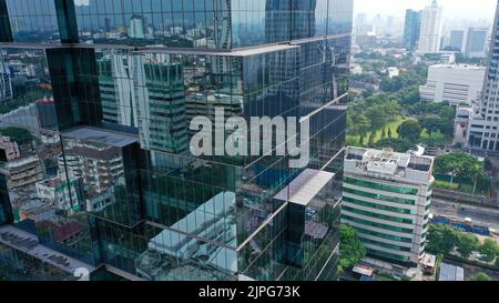 Survol vertical des drones parmi les gratte-ciels futuristes modernes du centre d'affaires de Jakarta City, reflet du coucher de soleil dans une façade en verre brillant Banque D'Images