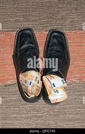 chaussures mâles noires sur tapis farcies de 50 billets en euros Banque D'Images