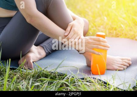 Une jeune femme méconnue est assise sur un tapis de yoga et tient une bouteille d'eau. Une bouteille d'eau dans la main d'une femme athlète Banque D'Images