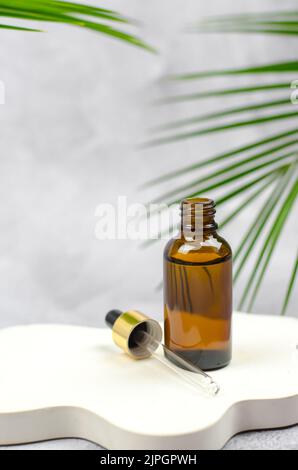 Huile essentielle naturelle sur un podium blanc dans une bouteille ouverte. Sérum dans un flacon en verre avec une pipette. Banque D'Images