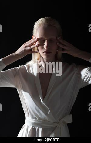 Jeune femme blonde albino faisant la gymnastique faciale automassage et des exercices rajeunissants sur fond noir. Banque D'Images