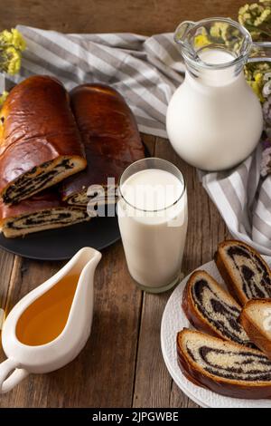 Rouler avec des graines de pavot et un verre de lait. Nourriture sur table. Pâtisseries sucrées. Pain de levure simple fait maison avec garniture. Petit déjeuner sur une table en bois. Lactose et gluten. Bains bouillonnants au miel Banque D'Images