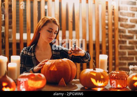 Jeune femme faisant la citrouille d'Halloween Jack-o-lanterne.Les mains de femmes coupantes des citrouilles avec un couteau Banque D'Images