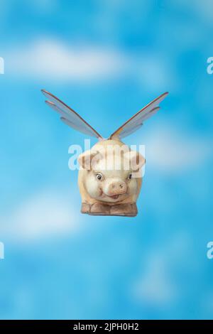 Banc de cochon en céramique avec ailes d'insectes volant sur fond bleu de skyes, vue de face. Quand les cochons volent la métaphore. Banque D'Images