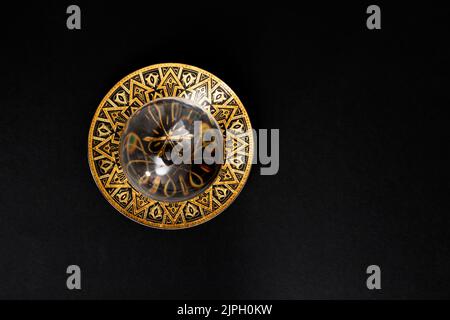 Boule de lentille défocalisée sur un plateau métallique doré, isolée sur fond noir. Pose à plat de près. Banque D'Images