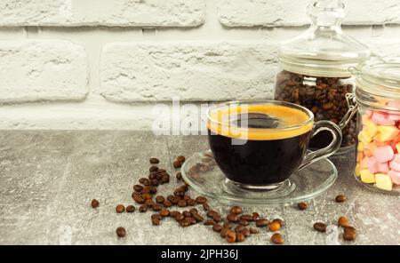 Café noir expresso dans un verre avec crème et guimauves dans un pot en verre. Grains de café sur une surface murale en brique grise et blanche avec espace de copie Banque D'Images