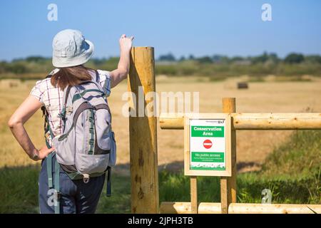 Vue arrière du rambler/randonneur femelle dans la campagne du Royaume-Uni par le panneau « zone de conservation, pas d'accès public » le jour chaud ensoleillé dans la vague de chaleur du 2022 août. Banque D'Images