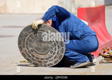 Ouvriers en uniforme bleu sur la trappe d'égout ouverte d'une rue. Concept de réparation des eaux usées, des services publics souterrains, du système d'approvisionnement en eau, de la pose de câbles Banque D'Images