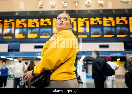 Les passagers pleins d'espoir regardent le panneau des départs à la gare d'Euston pendant une autre journée de grève ferroviaire par le syndicat des travailleurs ferroviaires de la RMT, le 18th août 2022, à Londres, en Angleterre. Plus de 45 000 travailleurs du rail sont sortis d'affilée au sujet de salaires, d'emplois et de conditions. Les passagers des trains ont été confrontés à davantage de perturbations, avec seulement 20 % des services en cours jeudi, mais deux jours supplémentaires d'action industrielle impliquant des employés d'autobus et de métro. Banque D'Images