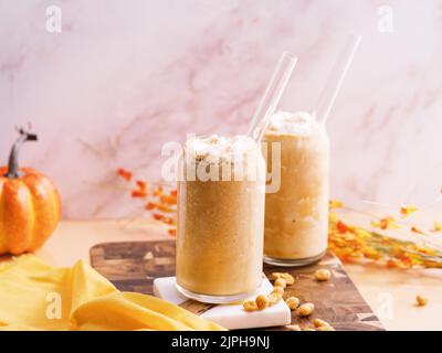 Gros plan de deux tasses en verre de milk-shakes à la citrouille avec une paille sur un panneau en bois Banque D'Images