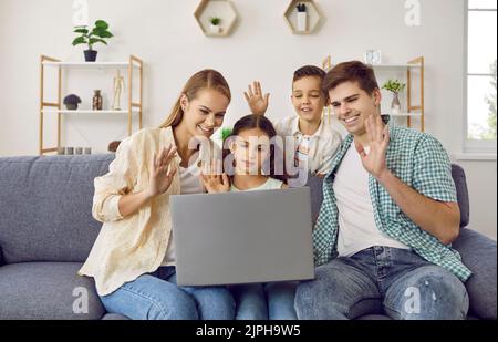 Bonne famille assise sur le canapé, passer un appel vidéo et se faire un bonjour sur le PC portable Banque D'Images