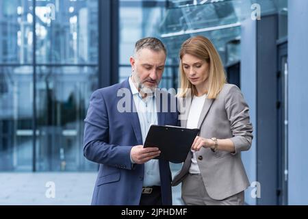 Deux collègues se concentrent et réfléchissent, un homme et une femme en vêtements d'affaires discutent de stratégie d'affaires, un groupe de gens d'affaires à l'extérieur d'un immeuble de bureaux Banque D'Images
