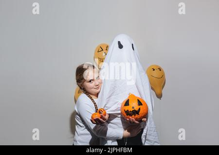 Joyeux Halloween. Une fille épouse un fantôme dans un costume blanc et tient une citrouille orange. Boules orange peintes. Différentes émotions de joie, de colère, de rire. Design festif, concept de fête. Mise au point sélective douce Banque D'Images