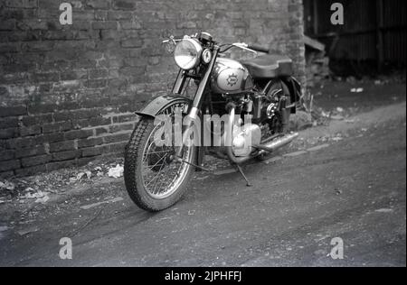 1950s, historique, une moto britannique de BSA de l'époque garée sur un chemin de terre à l'extérieur d'un ancien entrepôt de briques, Angleterre, Royaume-Uni. Badge RAC en métal sur la fourche avant. Fondée en 1861 sous le nom de Birmingham Small Arms Company Ltd, pour la production d'armes à feu, une division moto a été créée en 1903, et la première moto a été lancée en 1910. En 1950s, BSA Motorcycles était le plus grand fabricant de motos au monde. Banque D'Images