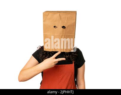 Jeune femme portant un sac en papier sur sa tête tenant la main comme des ciseaux Banque D'Images