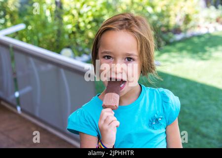 Fille portant un t-shirt vert, ayant une glace au chocolat au lait, dans la rue, en été. Crème glacée, popsicle, manger, sucré et concept d'été. Banque D'Images