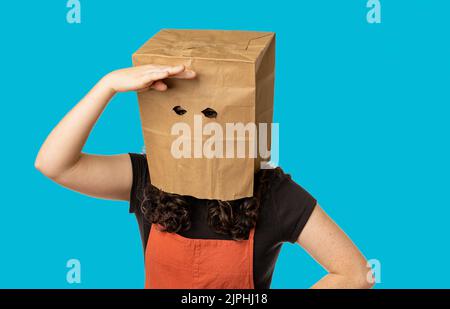 Femme portant un sac en papier au-dessus de sa tête regardant autour Banque D'Images