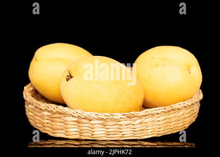 Trois abricots jaune vif juteux d'ananas dans un bol de paille, macro isolé sur un fond noir. Banque D'Images