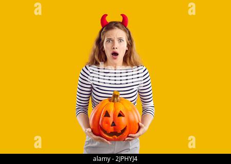 Portrait d'une jeune femme choquée et effrayée tenant la citrouille d'Halloween sur fond orange. Banque D'Images