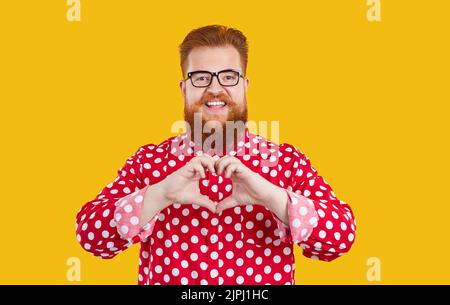 Portrait de gai drôle barbu gras homme montrant l'amour geste isolé sur fond orange. Banque D'Images