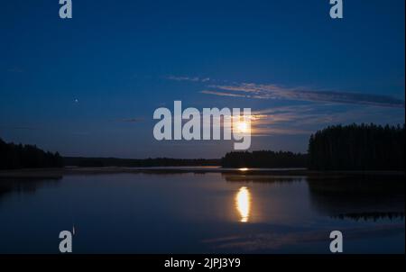 Nuit clair de lune au bord du lac. Pleine lune et planète Jupiter dans le ciel et réfléchissant sur la surface de l'eau. Banque D'Images