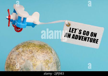 Concept de voyage et d'affaires. Sur un fond bleu, un globe et un avion avec un signe - allons sur une aventure. Globe hors foyer. Banque D'Images