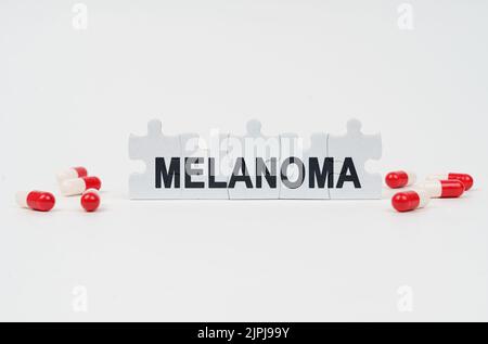 Concept médical. Sur une surface blanche sont des comprimés et des puzzles avec l'inscription - MÉLANOME Banque D'Images