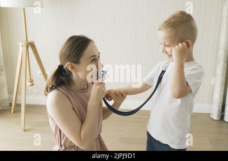 Le garçon écoute par un stéthoscope ce que sa mère lui dit. Jeux pour enfants Banque D'Images