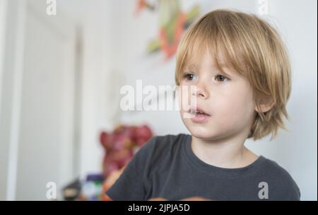 Portrait en gros plan d'un enfant blond mignon avec expression pensive à la maison. Banque D'Images