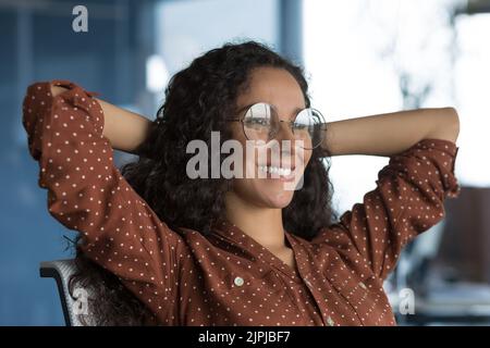 Jeune belle femme d'affaires arabe se reposant dans le bureau souriant, femme travaillant en lunettes a soulevé ses mains sur le titre, se reposant et heureux avec succès, photo de gros plan Banque D'Images