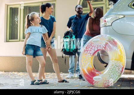 Famille et amis mixtes partant en vacances, en chargeant des sacs gonflables et de chariot dans le coffre du véhicule pour voyager pendant les vacances d'été. Aller à la destination balnéaire avec des gens souriants. Banque D'Images