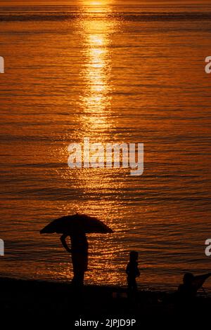 Silhouette d'homme debout sous un parapluie à la plage de la mer. Vue magnifique sur le coucher de soleil orange. Vacances d'été Banque D'Images