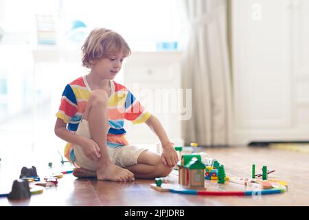 Les enfants jouent avec un chemin de fer en bois. Enfant avec train jouet. Jouets éducatifs pour les jeunes enfants. Petit garçon construisant des voies de chemin de fer sur le sol blanc Banque D'Images