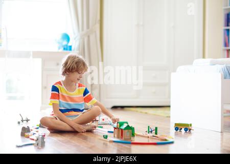 Les enfants jouent avec un chemin de fer en bois. Enfant avec train jouet. Jouets éducatifs pour les jeunes enfants. Petit garçon construisant des voies de chemin de fer sur le sol blanc Banque D'Images