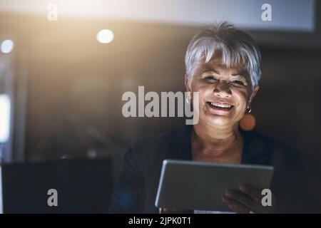 Accès à tout pour une nuit de travail productive. Une femme d'affaires mature utilisant une tablette numérique tard dans la nuit dans un bureau moderne. Banque D'Images
