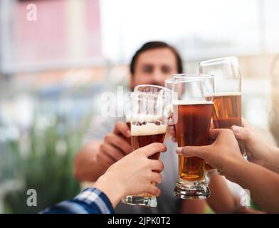 Au premier tour, un groupe de jeunes collègues d'affaires méconnus ayant un toast festif avec de la bière autour d'une table. Banque D'Images