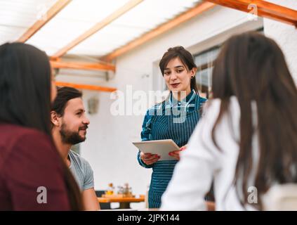 Qu'est-ce que vous allez avoir aujourd'hui. Un groupe de jeunes collègues d'affaires joyeux commandant de la nourriture et des boissons d'un serveur tout en étant assis à un Banque D'Images
