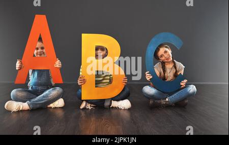 Commencez par les notions de base. Portrait studio d'un groupe diversifié d'enfants tenant des lettres de l'alphabet sur un fond gris. Banque D'Images