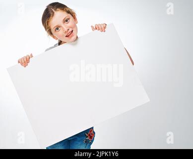 Je partage votre message. Photo studio d'une adorable petite fille portant un écriteau vierge. Banque D'Images