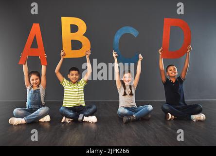 Maintenant je connais mon ABC. Portrait studio d'un groupe diversifié d'enfants tenant des lettres de l'alphabet sur un fond gris. Banque D'Images