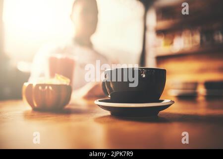 Commencez votre journée par une tasse de perfection. Une tasse de café fraîchement préparé sur une table en bois d'un restaurant. Banque D'Images