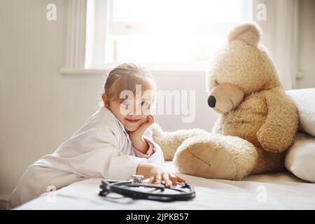 Une adorable petite fille vêtue comme médecin et traitant son ours en peluche comme une patiente. Banque D'Images