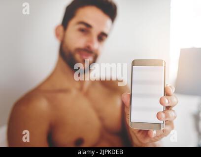 Le meilleur endroit pour afficher. Portrait court d'un beau jeune homme tenant un téléphone portable dans sa chambre à la maison. Banque D'Images