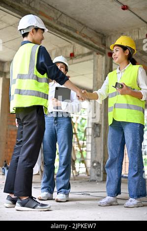 Un jeune homme asiatique beau et jeune ingénieur civil se secouant la main avec une femme inspecteur de construction sur le chantier de construction. Banque D'Images