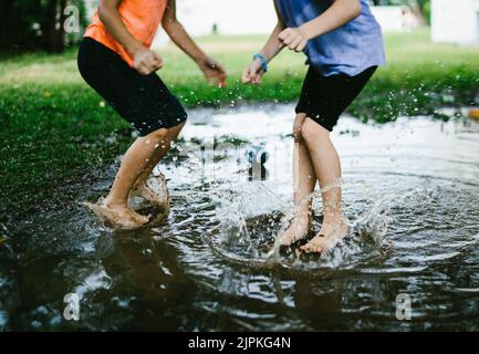 Deux enfants sautent dans une flaque de pluie sur un terrain vert Banque D'Images