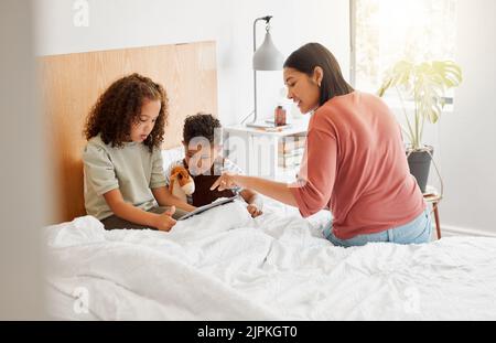 Mère et enfants apprenant sur la tablette numérique en ligne, la famille se liant à Internet dans la chambre et regarder des films dans le lit à la maison. Garçon et fille Banque D'Images