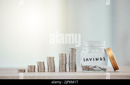 Financer, budgétiser et économiser de l'argent ou des pièces en déposant de la monnaie, de l'argent et des pièces de monnaie dans un pot en verre sur l'arrière-plan de l'espace de copie. Gros plan de la pile, empilée Banque D'Images