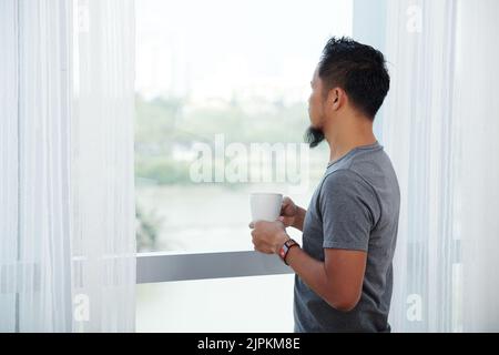 Homme buvant son café du matin et regardant par la fenêtre Banque D'Images