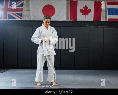 Un professionnel de la tenue de karaté étudiant et de se préparer à la pratique dans un dojo ou un club. Femme athlète d'art martial MIX nouant la ceinture à l'entraînement pour un combat Banque D'Images