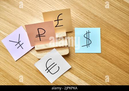Des cartes en papier multicolores avec des signes de devises mondiales répandues se trouvent sur une table en bois. Vue de dessus du concept de devise forte Banque D'Images